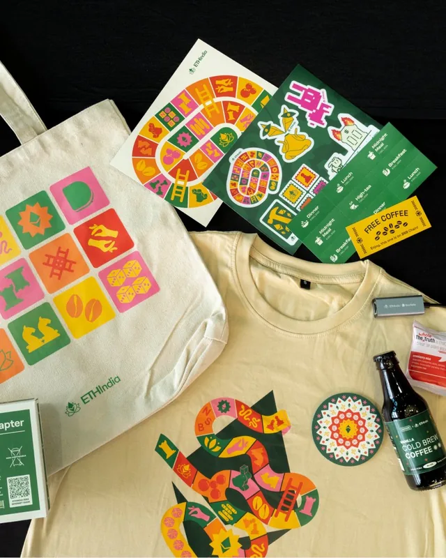 The ETHIndia 2024 tote bag, T-shirt and stickers laid out